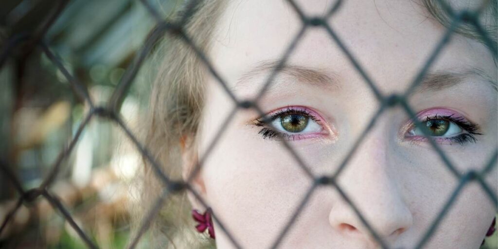 Beeld van een vrouw, met verdriet in haar ogen, achter een metalen hek - staat voor gevangen zijn in moderne slavernij en uitbuiting